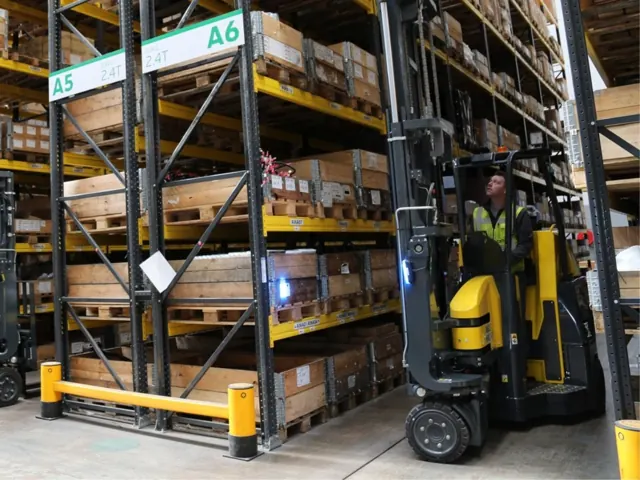Articulated forklift in a narrow aisle between loaded racks