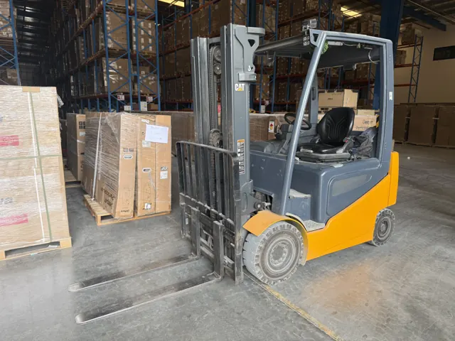 Electric counterbalance forklift beside stacked cartons in a warehouse
