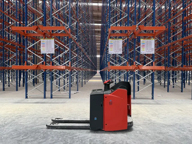 Red electric pallet truck in a high-bay racking aisle, front view