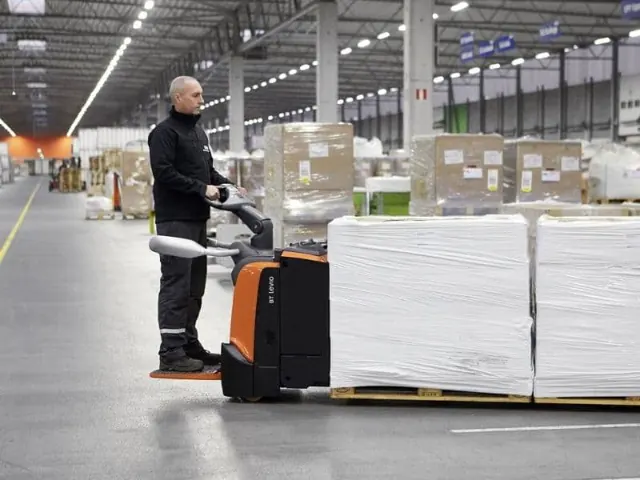 Operator moving a wrapped pallet with an electric pallet truck