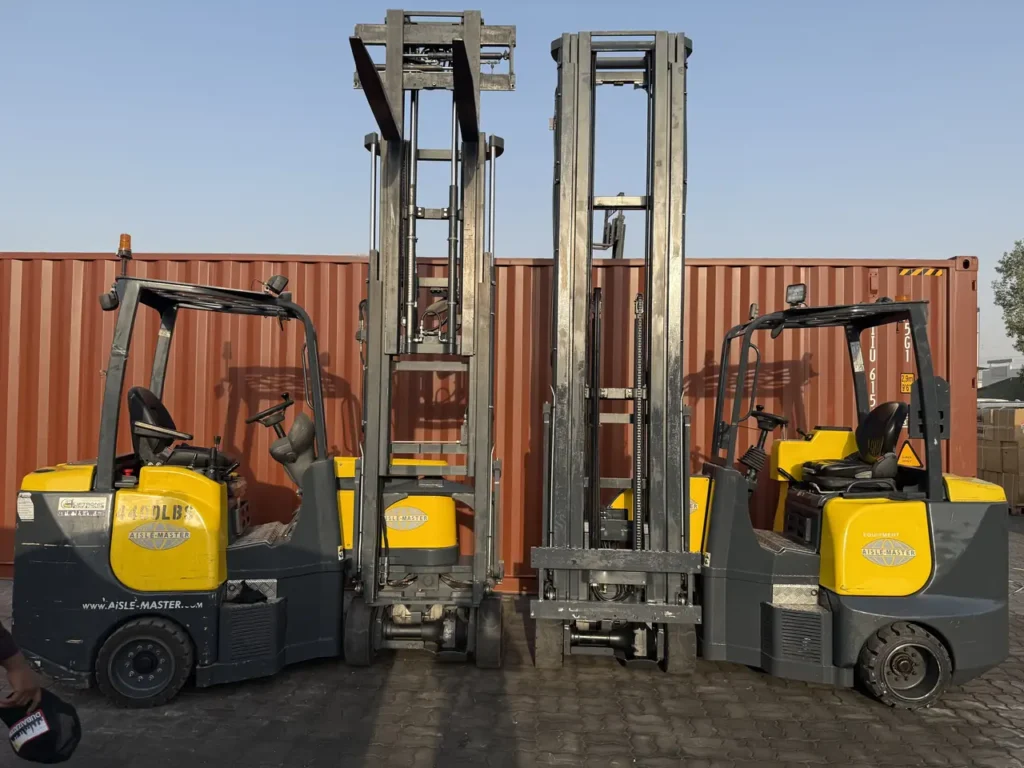 Two Aisle-Master articulated forklifts with raised masts beside shipping containers
