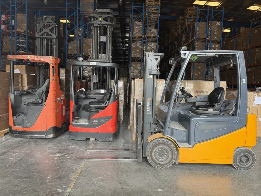 Two electric reach trucks and an electric counterbalance forklift parked in a racking warehouse